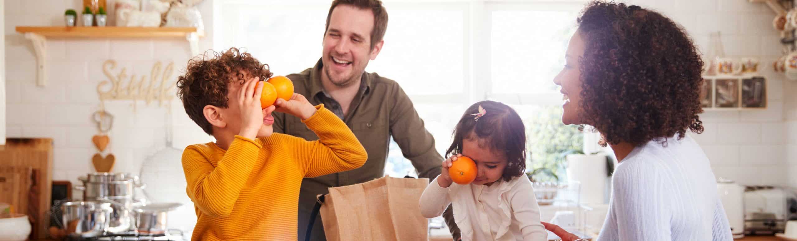 Parents and two kids playing with fruits on the kitchen counter