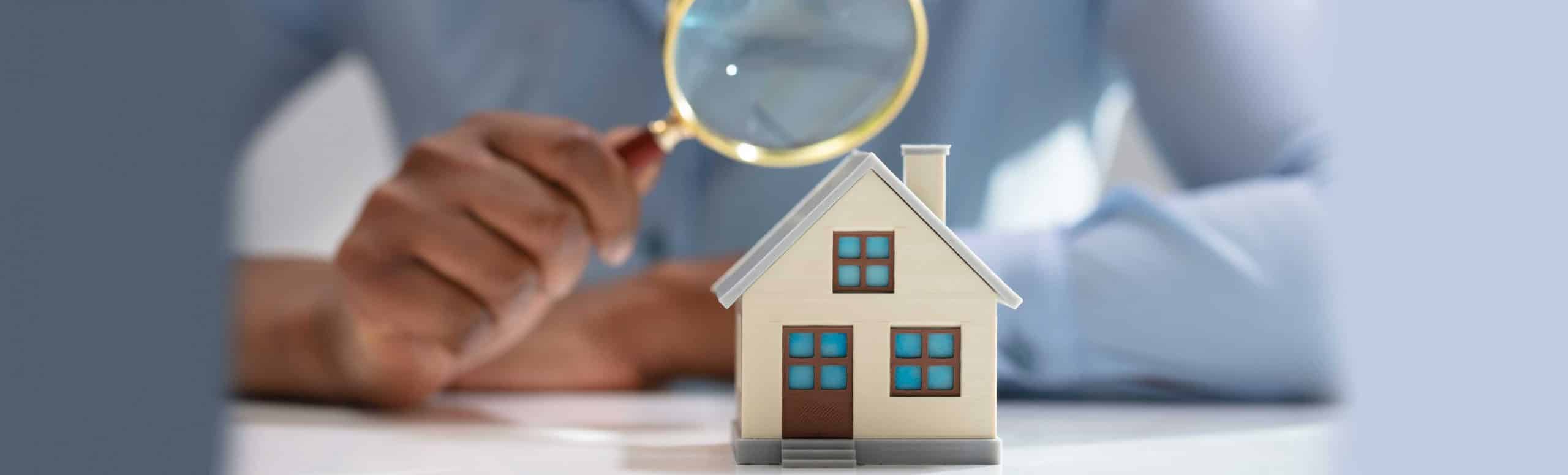 Person holding magnifying glass over a small toy house