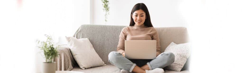 A girl sitting on a couch and reading something on her laptop
