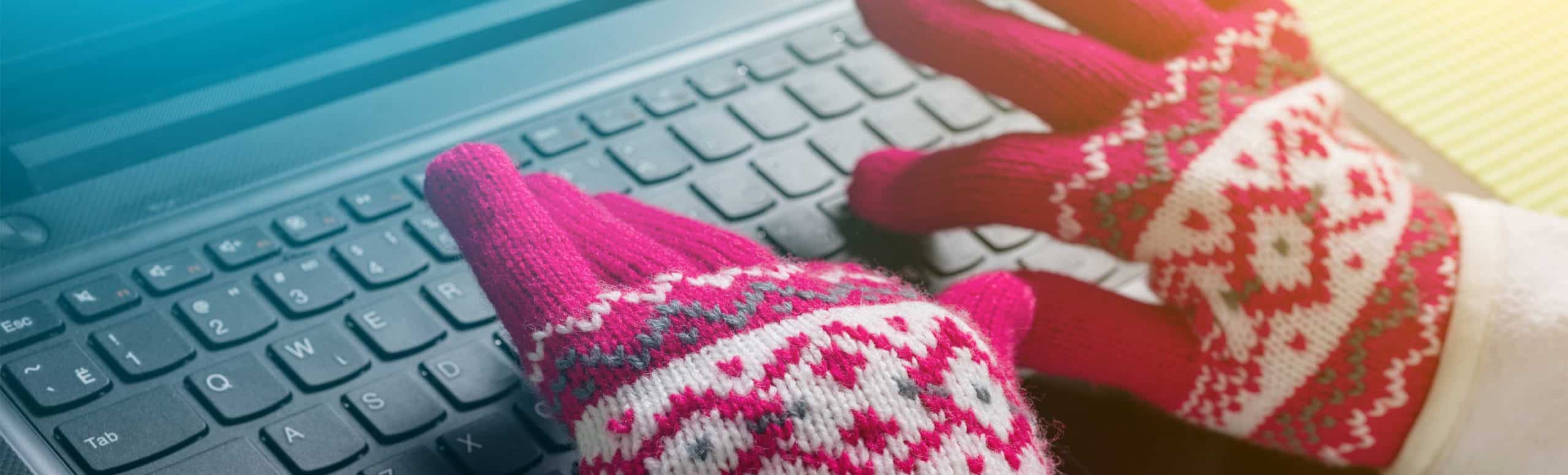 close of of hands in winter gloves typing on computer keyboard