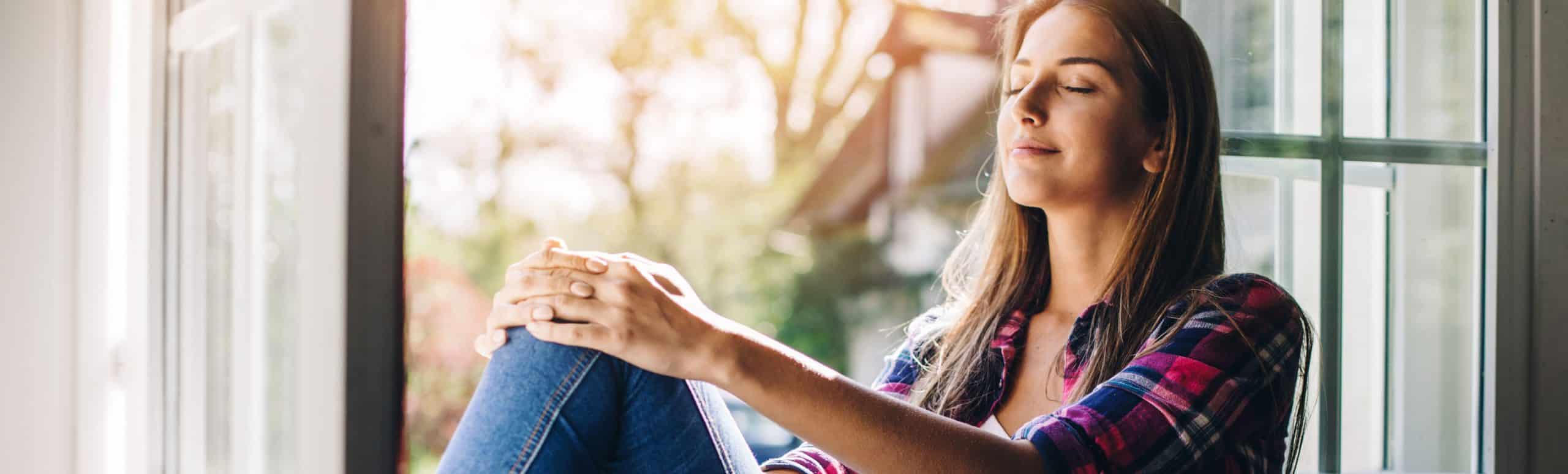 Woman right beside an open window enjoying the sun and fresh air