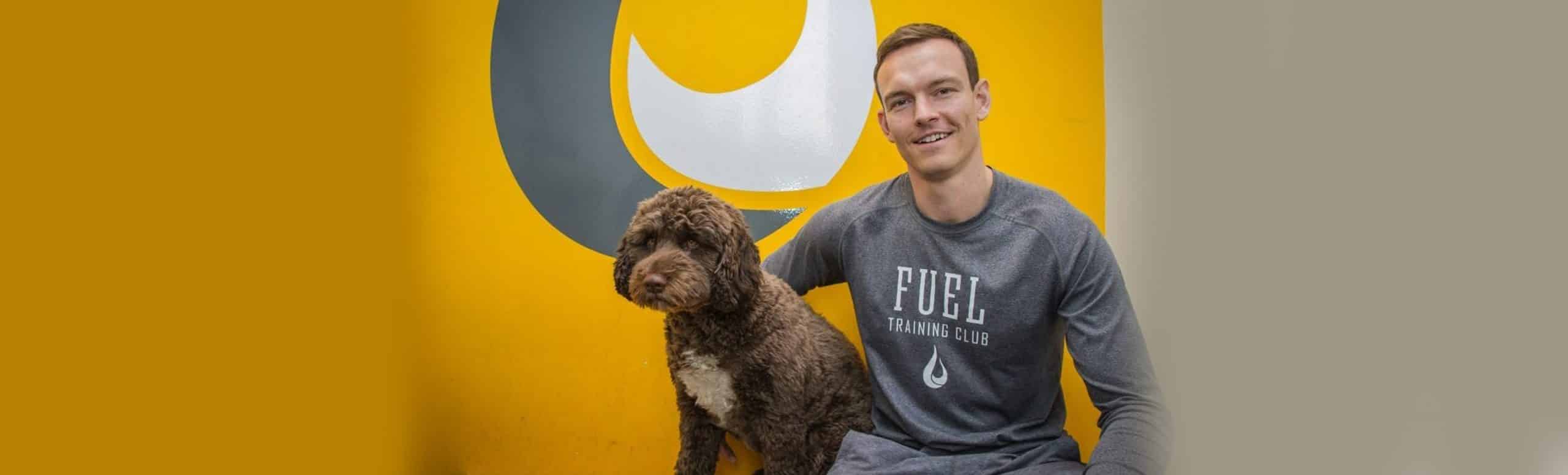 Male sitting in front of yellow wall with his brown dog.