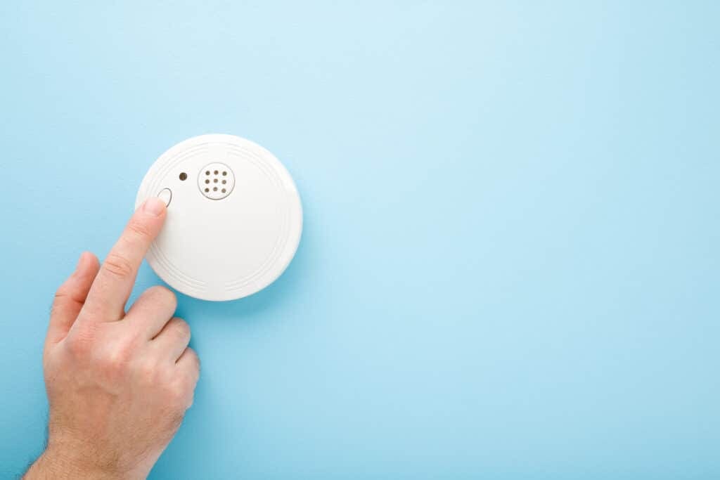 Finger touching new white plastic smoke alarm against a light blue background