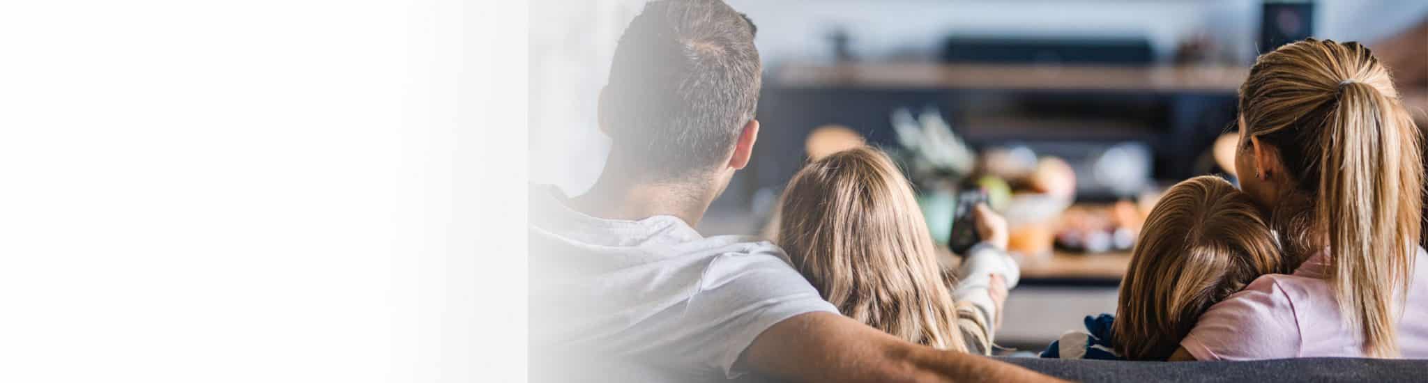 Family sitting on sofa facing TV. Little girl pointing remote