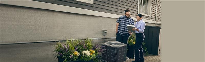 A technician showing information on a clipboard to a customer next to an AC unit